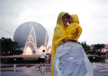 Mom and Max in ponchos with the fountain and big ball in the background.